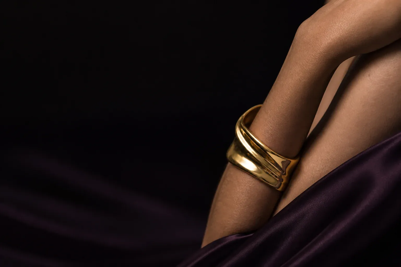 Sculptural gold cuff worn against aubergine silk