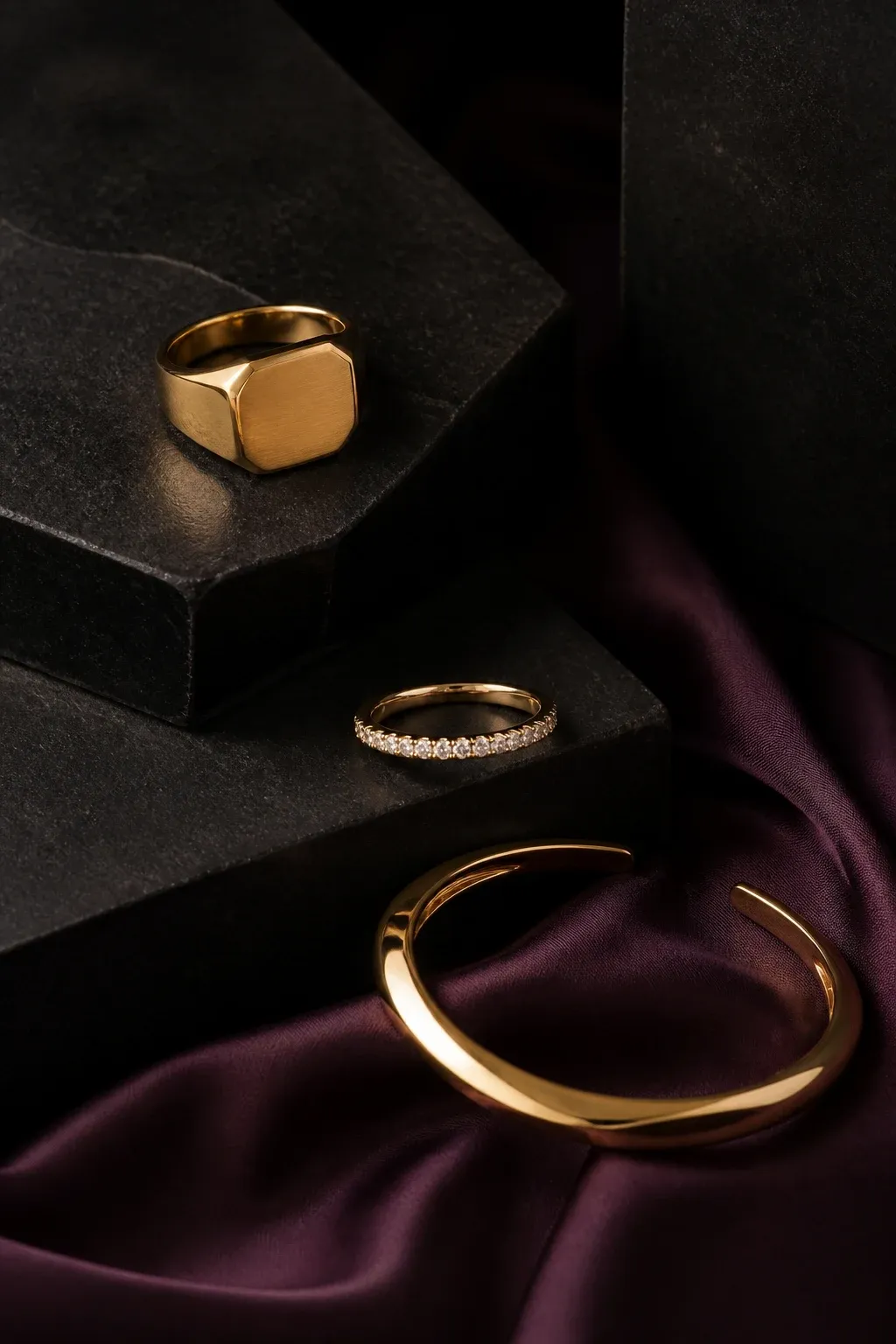 Three signature gold jewelry forms on black stone and aubergine silk